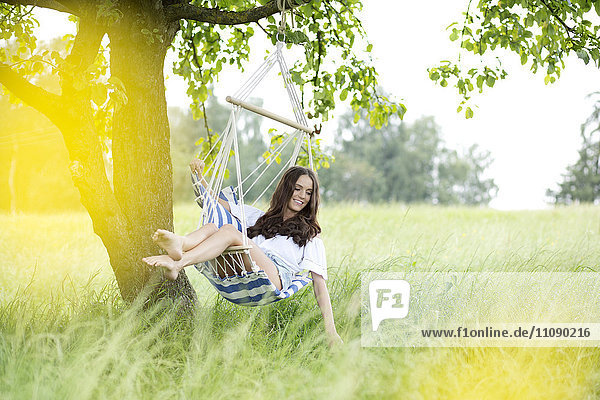 Glückliche Frau entspannt sich in einem Hängestuhl unter einem Baum