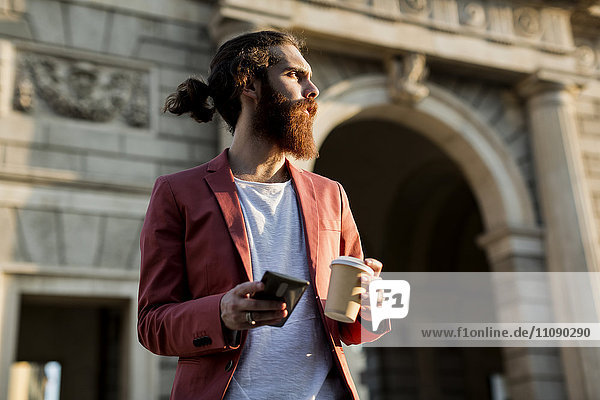 Young man with coffee and smartphone looking at distance