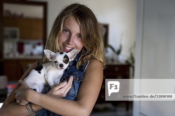 Smiling woman with dog on her arms at home