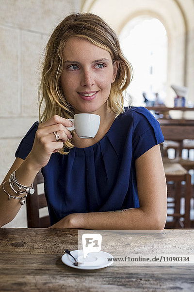 Porträt einer lächelnden blonden Frau beim Espresso-Trinken in einem Straßencafé