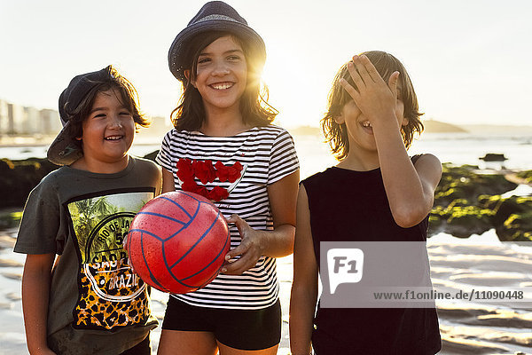 Three happy kids with ball on the beach at sunset