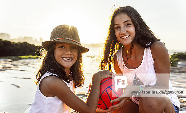 Two happy girls with ball on the beach at sunset