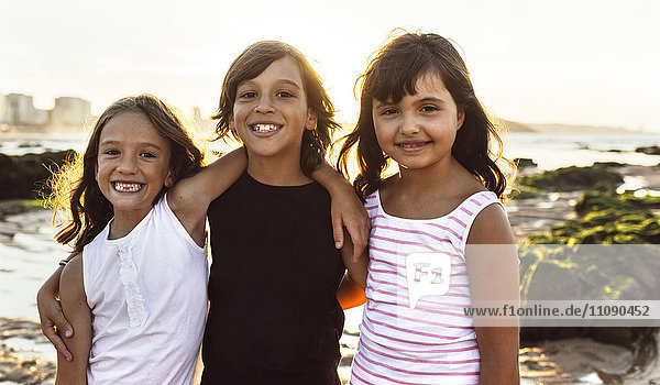 Porträt von drei glücklichen Kindern am Strand bei Sonnenuntergang