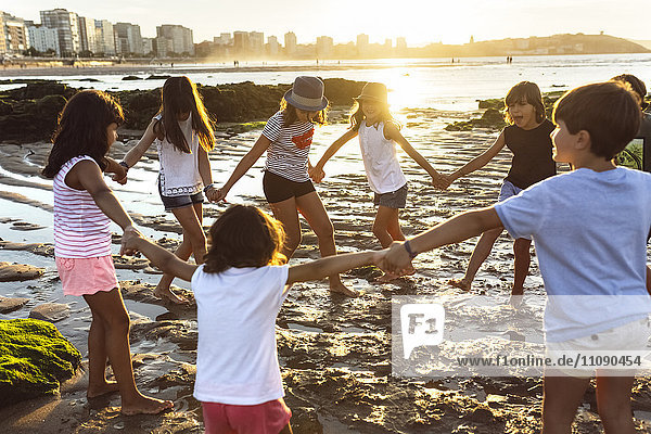 Kinder spielen Hand in Hand am Strand bei Sonnenuntergang