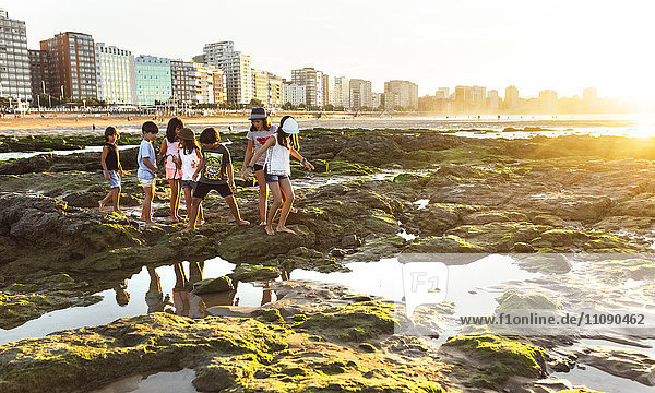 Kinder  die bei Sonnenuntergang am felsigen Strand spazieren gehen.