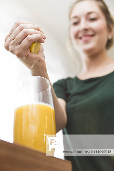 Frau  die Zitronensaft in ein Glas hausgemachten Smoothie drückt.