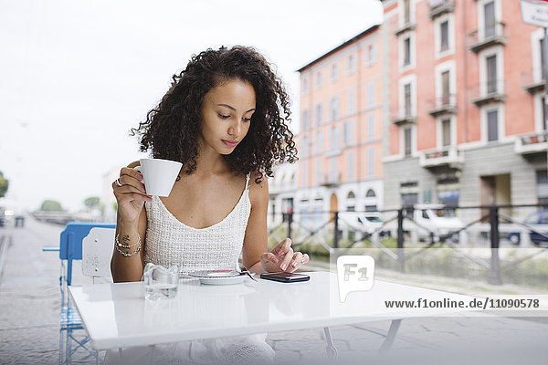 Junge Frau mit Tasse Kaffee über ihr Smartphone