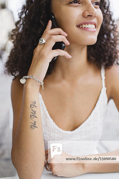 Lächelnde junge Frau mit Tattoo auf dem Unterarm am Telefon