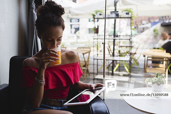 Junge Frau trinkt ein Glas Orangensaft in einem Coffee-Shop und schaut sich die Tablette an.