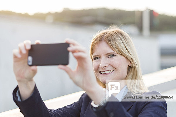 Portrait of smiling blond businesswoman taking selfie with smartphone