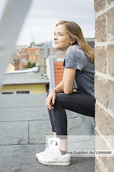 Smiling teenage girl sitting on roof top looking at distance
