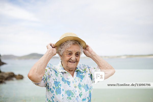 Portrait of smiling senior woman putting on straw hat