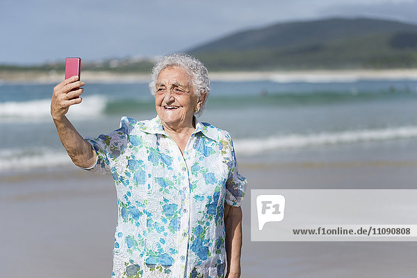 Lächelnde Seniorin nimmt Selfie am Strand auf