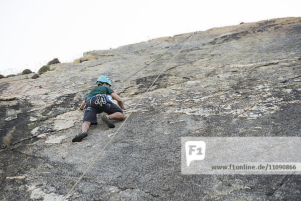Junger Mann klettert auf eine Felswand