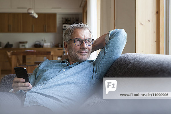 Mature man holding cell phone sitting on couch