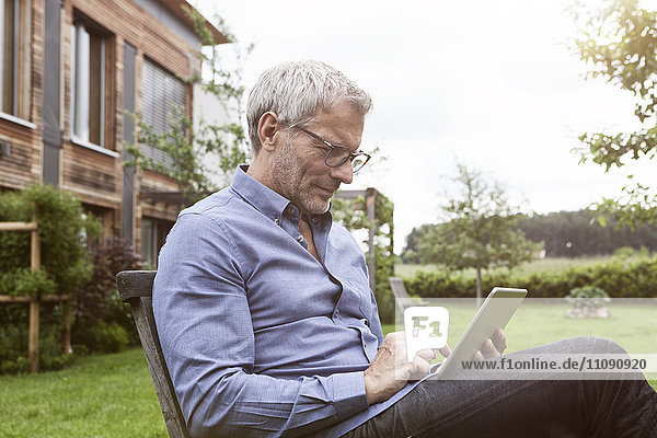 Erwachsener Mann mit digitalem Tablett im Garten