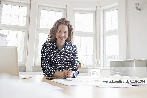 Porträt einer lächelnden Frau am Schreibtisch im Büro