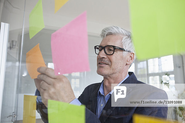 Businessman in office attaching adhesive notes at glass pane