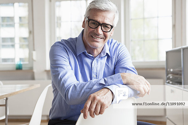 Portrait of smiling mature businessman sitting on chair in office