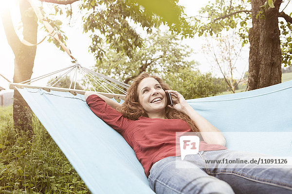 Smiling woman in hammock on cell phone