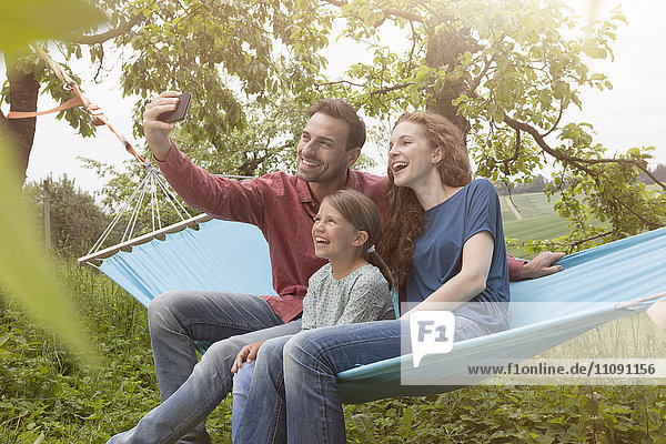 Glückliche Familie sitzt in Hammmock und nimmt sich einen Selfie.