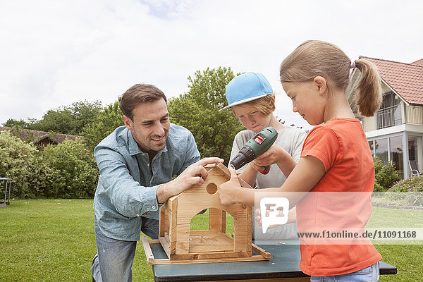 Vater und Kinder bauen gemeinsam ein Vogelhaus.