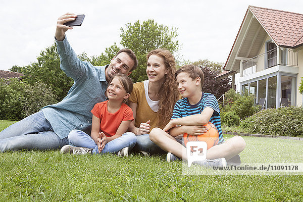 Lächelnde Familie,  die im Garten sitzt und einen Selfie nimmt.