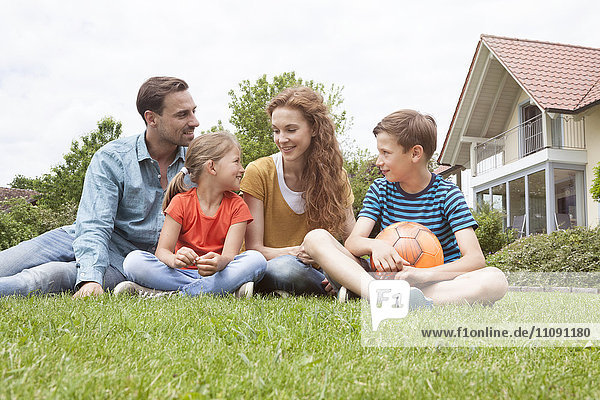Smiling family sitting in garden with football