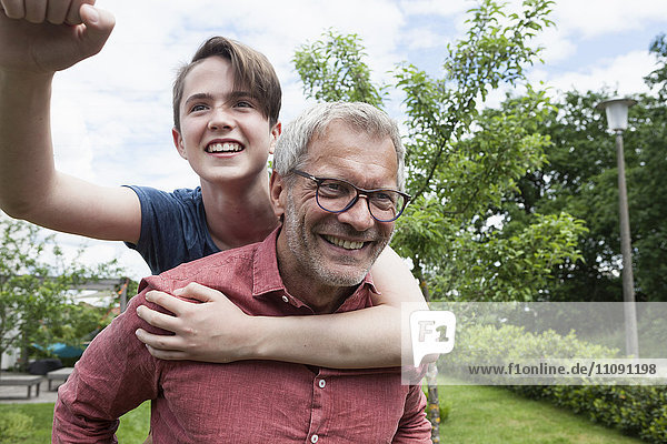 Glücklicher Vater trägt Sohn Huckepack im Garten