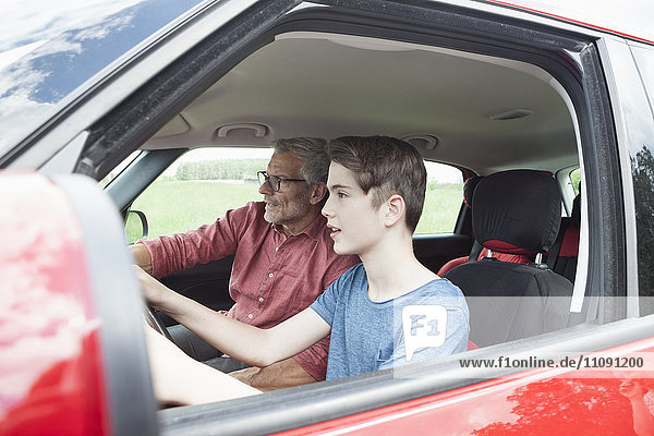 Vater unterrichtet den Sohn beim Autofahren
