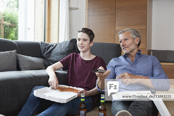 Father and son eating pizza and watching Tv together