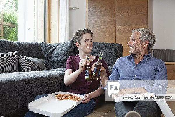 Father and son sitting on the floor clinking bottles in living room