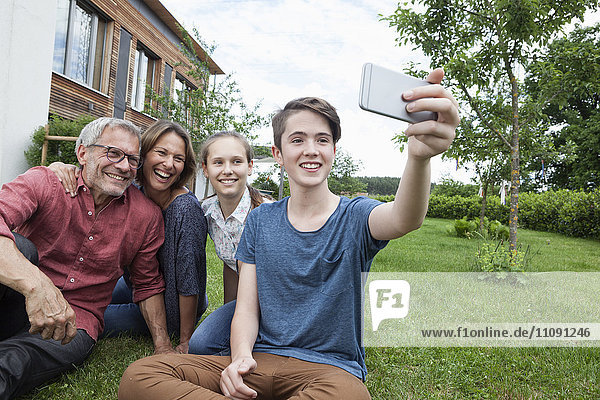 Teenager-Junge nimmt einen Selfie der glücklichen Familie  die im Garten sitzt.