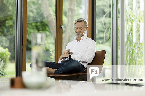 Mann auf Stuhl im Wohnzimmer mit Blick auf smartwatch