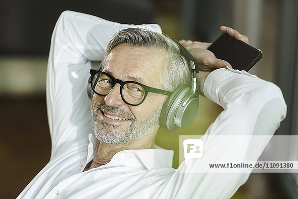 Porträt eines lächelnden Mannes mit grauen Haaren und Bart  der mit Kopfhörern Musik hört.