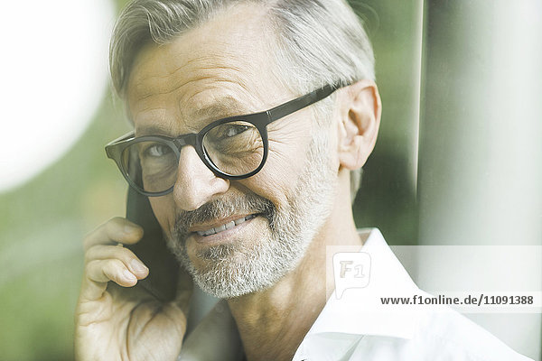 Porträt eines lächelnden Mannes mit grauen Haaren und Bart am Telefon