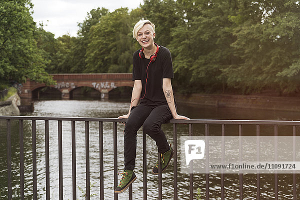 Laughing young woman sitting on railing in front of a canal