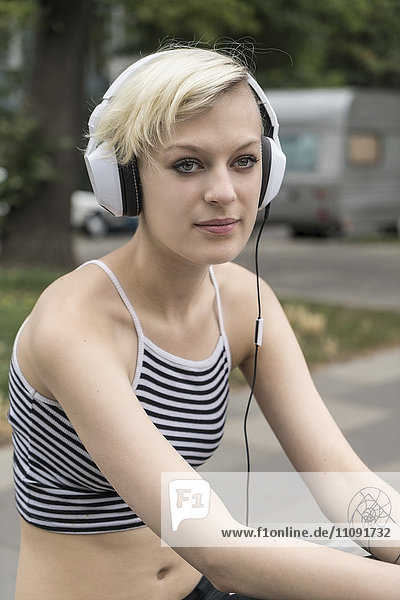 Porträt einer blonden jungen Frau beim Musikhören mit Kopfhörern