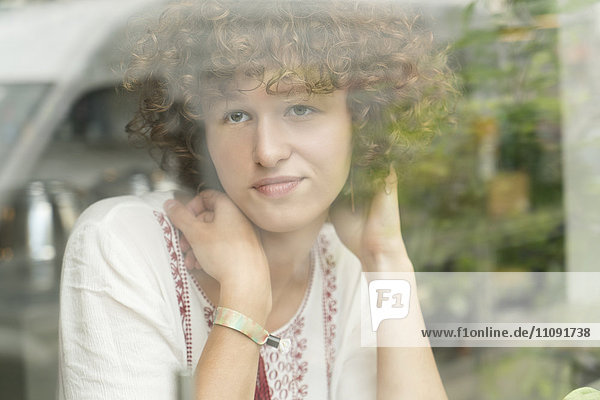Porträt einer träumenden jungen Frau,  die in einem Café sitzt und durchs Fenster schaut.