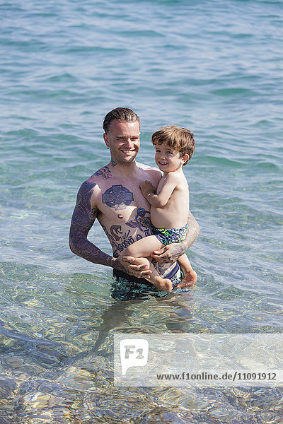 Tattooed man with his son in the sea