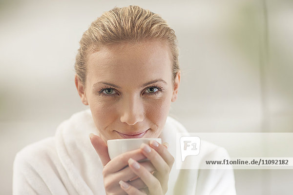 Porträt der lächelnden jungen Frau im Bademantel beim Tee trinken