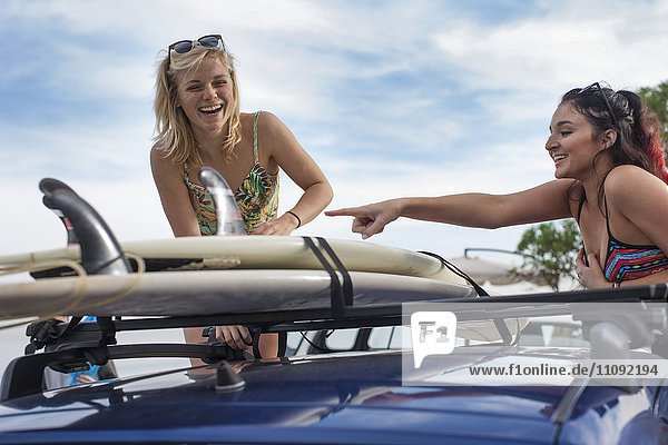 Zwei glückliche junge Frauen beim Auspacken von Surfbrettern im Auto