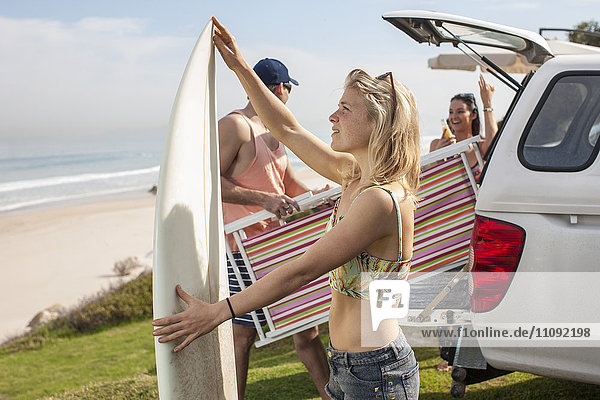 Freunde  die Surfbrett und Strandkorb aus dem Auto an der Küste nehmen.