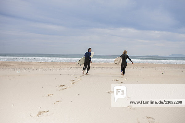 Paar mit Surfbrettern am Strand zu Fuß zum Meer