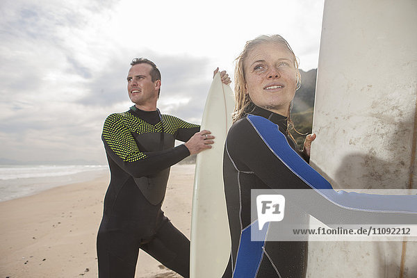 Paar mit Surfbrettern am Strand  die sich umsehen