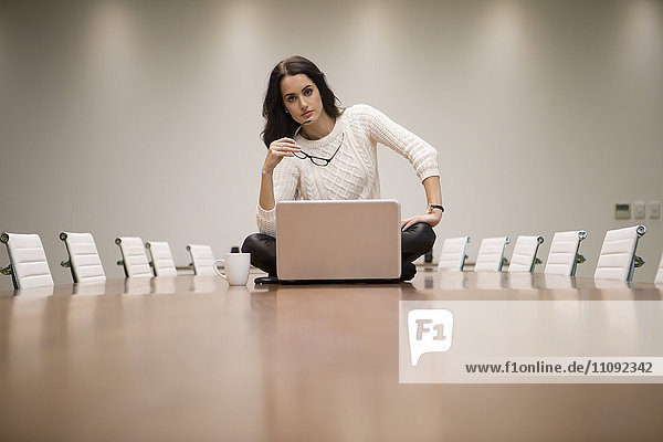 Geschäftsfrau mit Laptop auf Konferenztisch sitzend  mit Brille