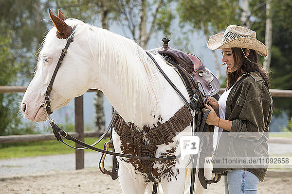 Young woman at riding stable saddling her horse