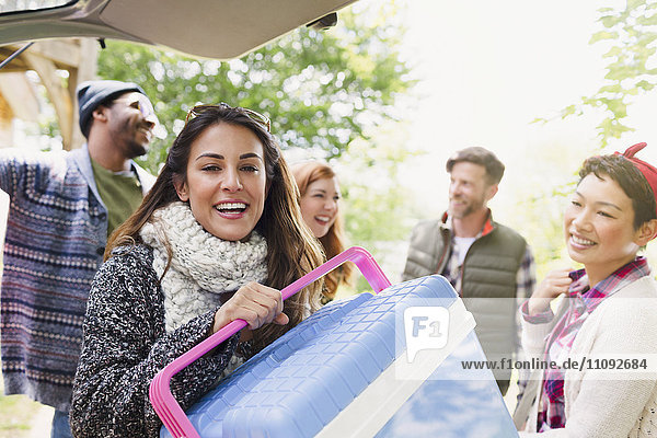 Portrait smiling woman with cooler at back of car with friends