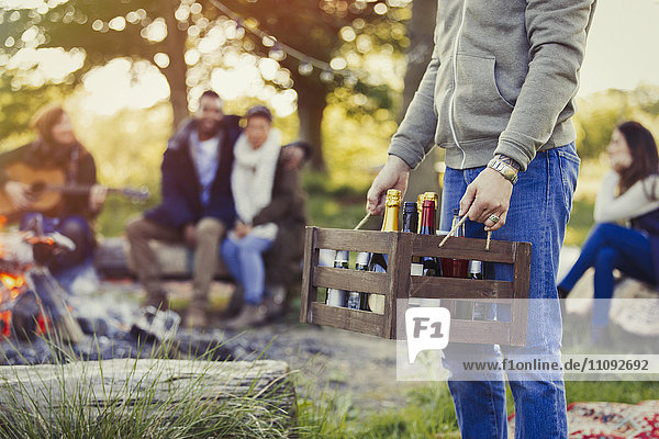 Mann mit Wein- und Bierkiste auf dem Campingplatz mit Freunden