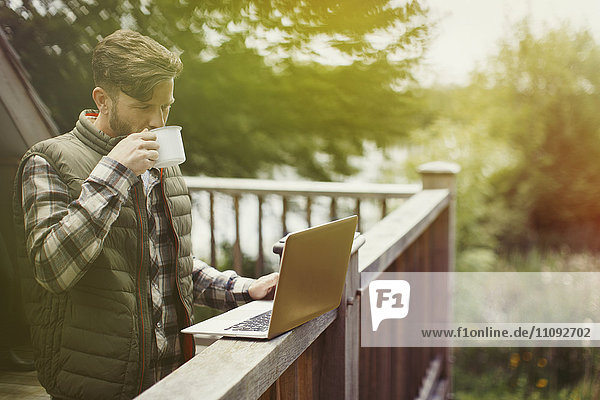Man drinking coffee and using laptop on cabin deck